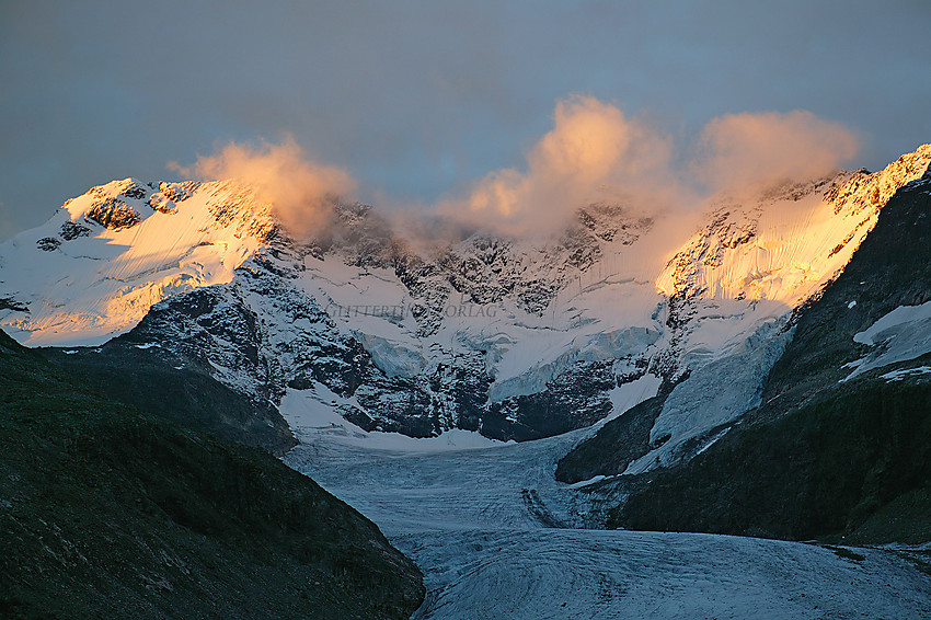 Flott morgenstemning like nedenfor Styggedalsbreen med selveste "Hurrungveggen" i soloppgang. Til venstre Styggedalstindane, mens Sentraltind og Vesle Skagastølstinden  skjuler seg i skyer. Helt oppe til høyre kan man ane Halls Hammer på Skagastølsryggen.