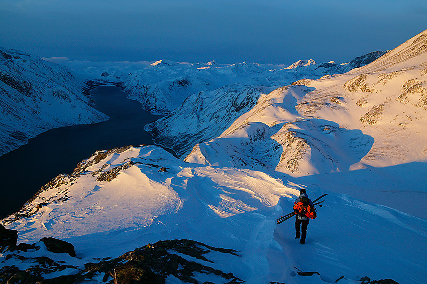 På vei ned Besseggen en tidlig vintermorgen med skiene i hendene. Gjende strekker seg som en skyggelagt kile dypt inn i Jotunheimen.