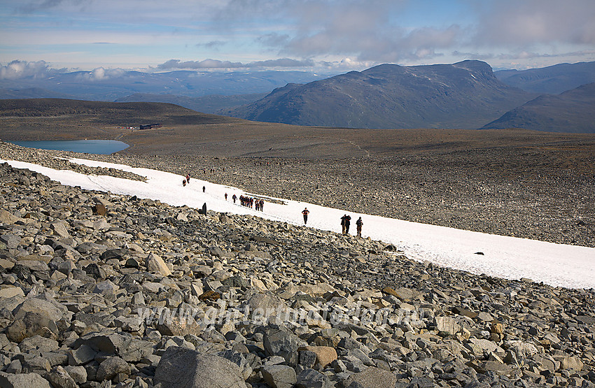 Guided tur til Galdhøpiggen. Fjellvandrerne er på vei fra Juvasshytta til kanten av Styggebreen, der taues tas på. Juvvatnet og Juvasshytta ses i bakgrunnen til venstre. Bak til høyre reiser Lauvhøe seg. 