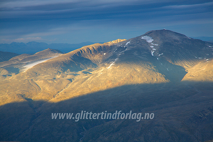 Sommerkveld på Galdhøpiggen med utsikt nordøstover mot Glittertinden (til høyre). Trollstein-Rundhøe er opplyst av kveldssola bakenfor til venstre, mens Rondane skimtes i horisonten.