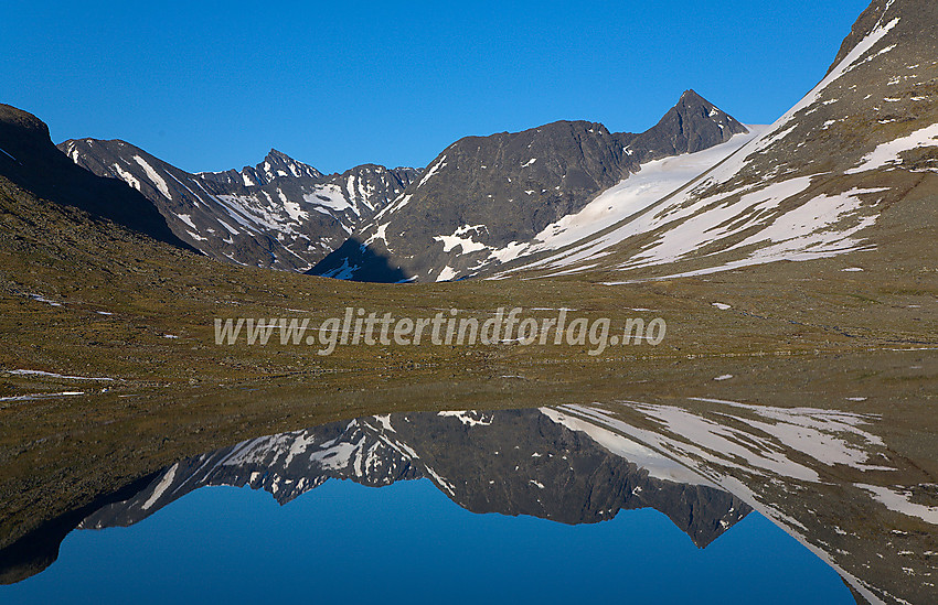 Semelholstinden (2147 moh) speiler seg i Leirvatnet en sommerkveld. Urdadalsryggen ses i bakgrunnen, og Store Hellstugutinden (2346 moh) stikker opp bak for denne igjen.