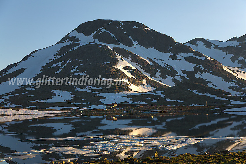 Stehøe (1885 moh) speiler seg i Leirvatnet en sommerkveld med Leirvassbu til sine føtter, som nyter de siste solstrålene.