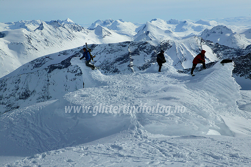 På toppen av Galdhøpiggen (2469 moh). Styggehøe (2213 moh) bakenfor. I bakgrunnen ses bl.a. Hellstugutindane, Semeltinden og Semelholstinden. Morten, Tor Erik og Pål poserer på den nedsnødde hytta på toppen.