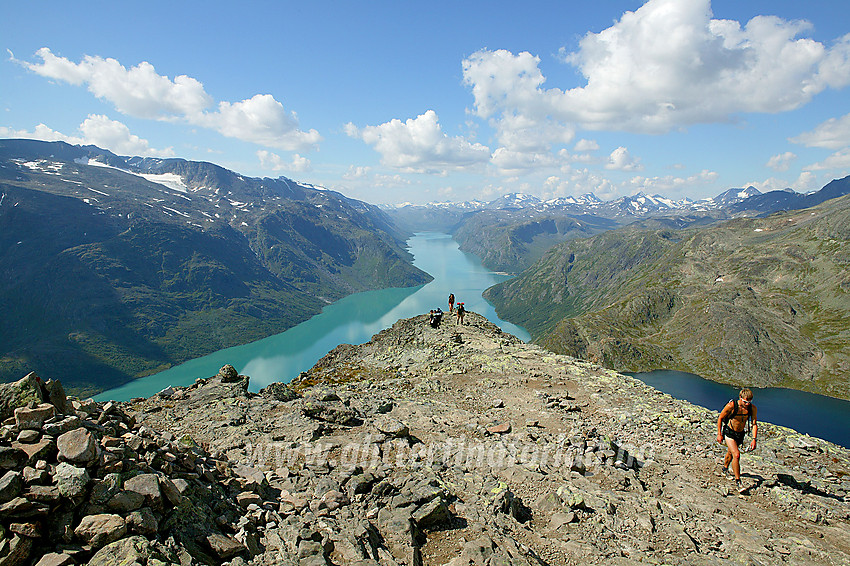 Fjellvandrere på rekke og rad som akkurat har kommet opp den bratteste delen av Besseggen. I bakgrunnen ser man dypt inn i Jotunheimen med Gjende som selve livsnerven.