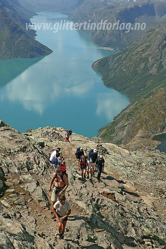 Fjellvandrere på lang rekke i den ovre del av Besseggen. Gjende i bakgrunnen.