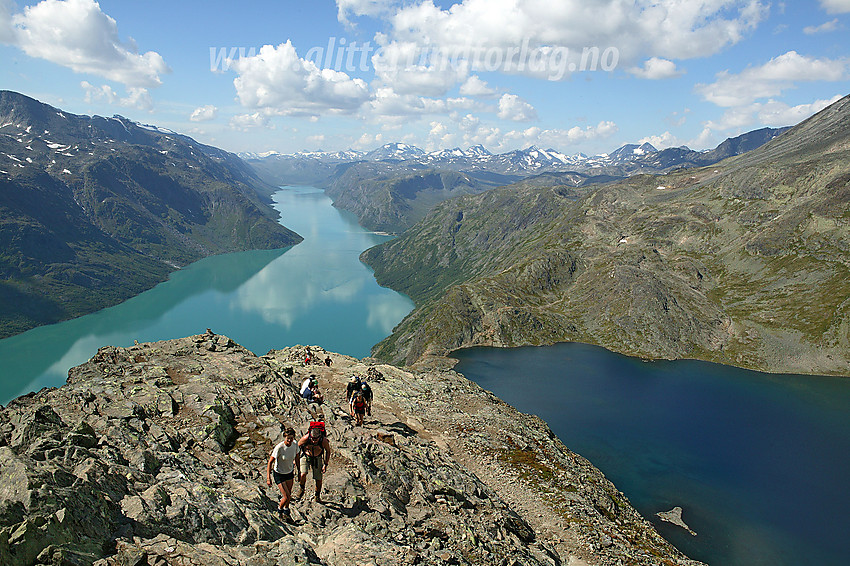 Fjellvandrere på vei opp Besseggen med det klassiske panoramaet med bregrønne Gjende til venstre og det langt mer sortblå Bessvatnet til høyre.