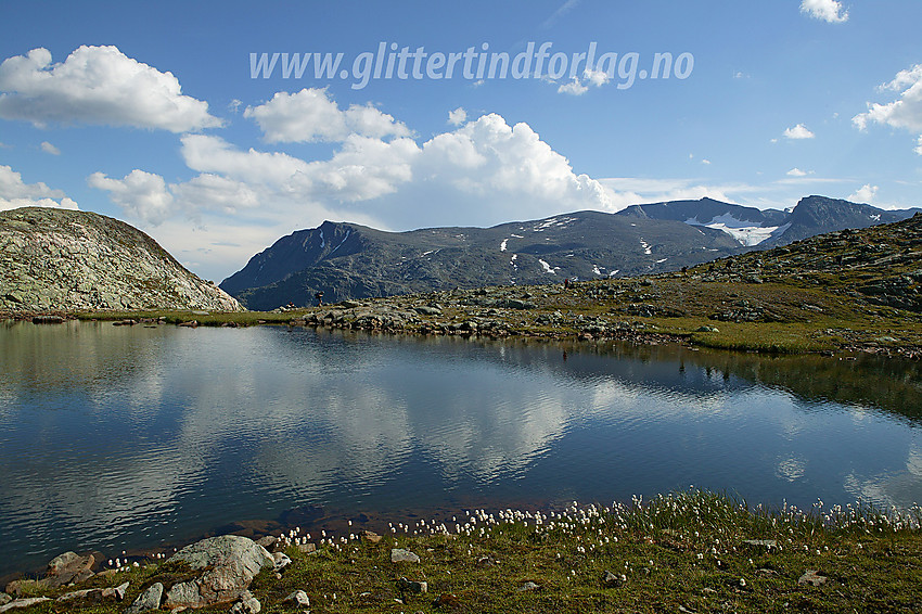 Ved Bjørnbøltjønne på ruta mellom Gjendesheim og Memurubu over Besseggen. På andre siden av tjernet ses flere fjellvandrere på stien og i bakgrunnen deler av Gjendealpene med f.v.: Bukkehåmåren, Kvassryggen, Høgdebrotet og Eggen.