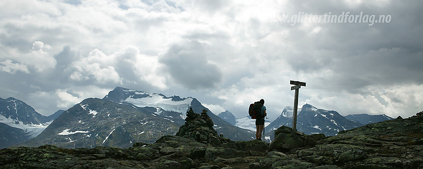 Fjellvandrer på Memurutunga der stien deler seg. En variant går ned det bratte Bukkelægret mens en annen slakere variant går over mot Storådalen. I bakgrunnen ruver Gjendealpene.