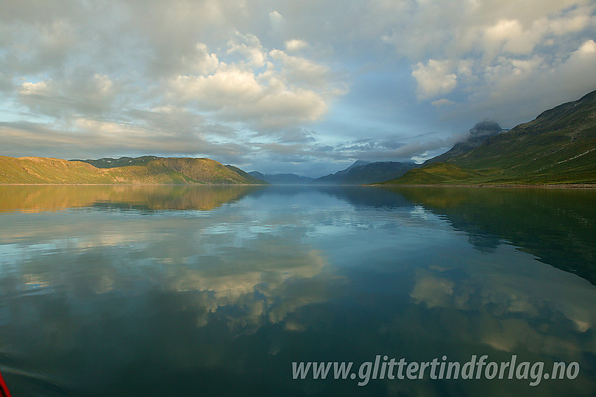 Fredfull padletur på Bygdin en tidlig sommermorgen. Vi er på vei vestover fra Bygdissundet mot Torfinnsbu. Ser du godt etter ser du padlepartneren som en liten prikk lenger inne på vannflata. Man blir liten som padler utpå Bygdin.