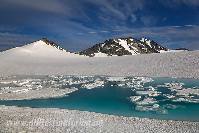 Ved et oppdemt bretjern på Vestre Memurubrean mot Søre (2189 moh), Nestsøre (2255 moh) og Store Hellstugutinden (2346 moh). Tjernet ligger tett innunder Hinnåtefjellet på nordsiden.