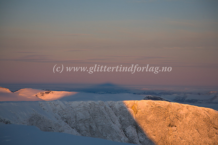 Glittertinden kaster en lang skygge like etter at sola har stått opp. I bakgrunnen Galdhøemassivet  (2283 moh.)