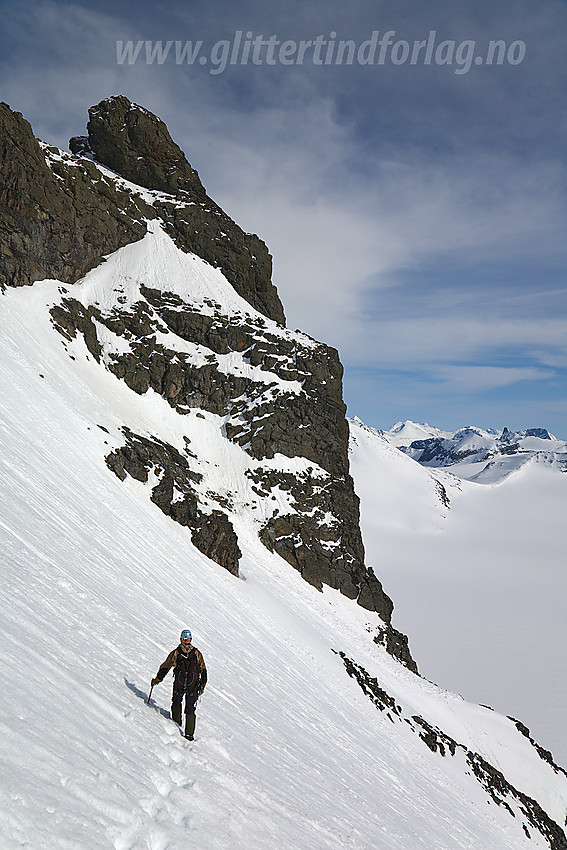 I sørvestflanken under Skardstinden med Nåle (2310 moh) i bakgrunnen. Her ser man godt direkteruta opp mot Nåle. Opp bratt snøfelt, og så langs snørampe fra venstre mot høyre oppunder bergveggen dit det øvre snøfeltet strekker seg lengst opp. Dernest kort bit med klyveklatring opp til foten av Nåle på venstre side.