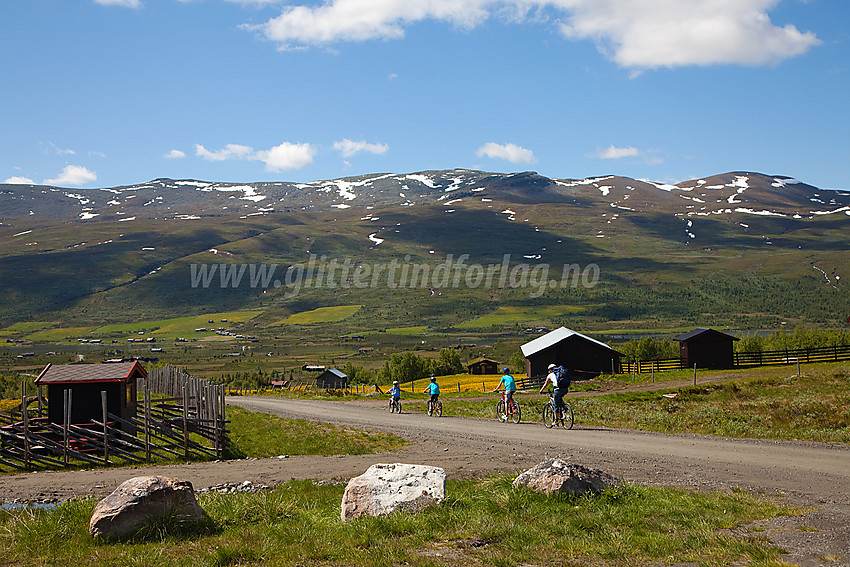 Syklister passerer forbi Syndinstøgo med Gilafjellet i bakgrunnen.