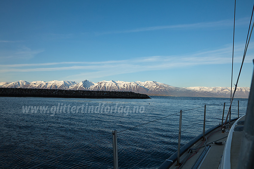 Vi har akkurat kastet loss og kjører ut gjennom moloen i Dalvik. På østsiden av fjorden ruver snødekte fjell opp i over 1000 moh.