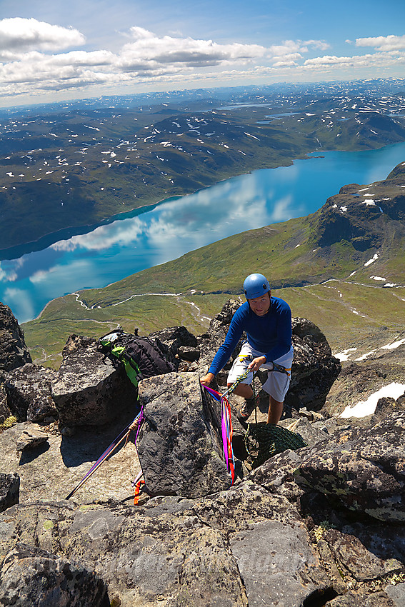 Gjermund gjør klar rappellfeste fra Midtre Torfinnstinden med Bygdin blinkende mer enn 1000 høydemeter lavere i bakgrunnen.