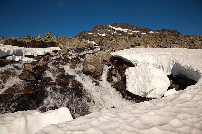 Snøfonn over elva fra Snøholsvatnet. Snøholstinden skimtes i bakgrunnen.