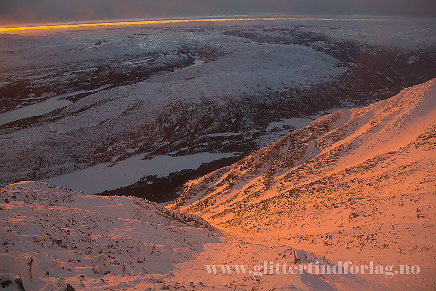 Ved masta på Gaustatoppen rundt solnedagn med utsikt vestover ned i Gausdalen med Aslaksatulvatn sentalt.