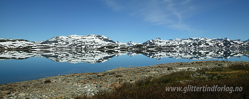 Ved Tyins østbredd mot Breikvamnosi. Lenger i bakgrunnen ses flere av Jotunheimens tinder som speiler seg i vannet.