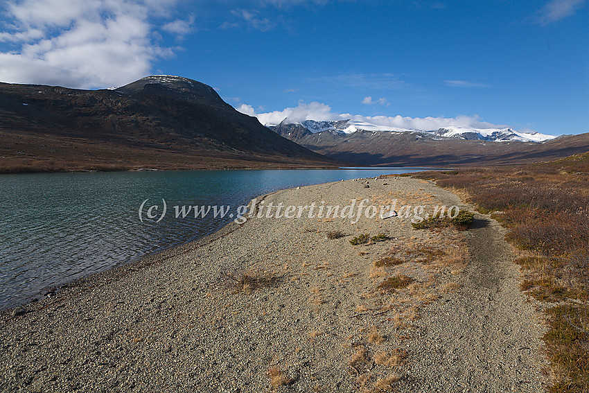 Ved nordbredden av Russvatnet ved en fin strand. I bakgrunnen Kollhøin nord for Besshøe. De snødekte fjellmassivene er bl.a. Surtningssue (i midten) og Styggehøbreatindane (til høyre).