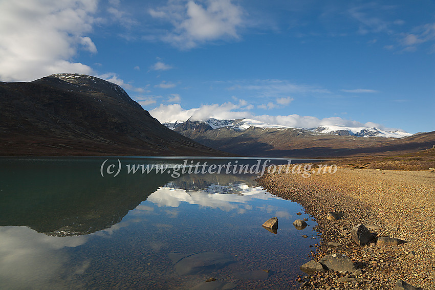 Ved nordbredden av Russvatnet ved en fin strand. I bakgrunnen Kollhøin nord for Besshøe. De snødekte fjellmassivene er bl.a. Surtningssue (i midten) og Styggehøbreatindane (til høyre).