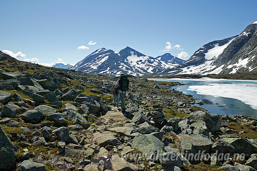 På vei langs merket sti med Øvre Høgvagltjønne på høyre side. Stien går fra Leirvassbu til Gjendebu eller Olavsbu. I bakgrunnen Skarddalseggje (2159 moh) og Skarddalstinden (2100 moh).