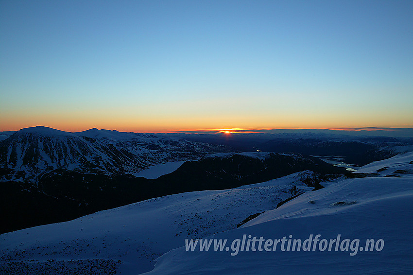 Solrenningen en maidag på toppen av Høgdebrotet (2226 moh). Omrisset til kjente størrelser som Besshøe, Nautgardstinden og Veslfjellet er lette å få øye på.