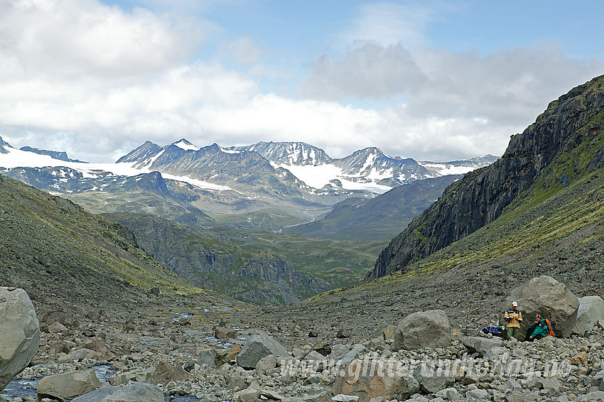 Pause ved stein like nedenfor Knutsholsbrean med utsikt nordover mot Memurubrean, Memurutindane og Memurudalen.