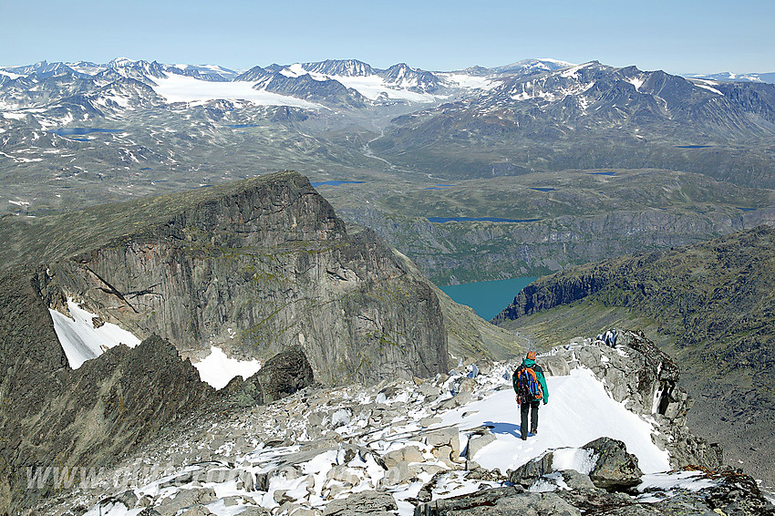 På vei ned nordryggen fra Store Knutsholstinden. I den umiddelbare forgrunn ses den kvasse ryggen nordover mot Nørdre Knutsholstinden. I bakgrunnen en rekke av Jotunheimens tinder og langt nede, mer enn 1300 meter, ses en flik av Gjendes grønne vannflate.