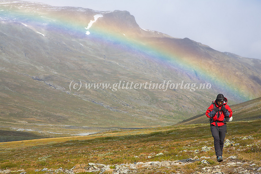 Fjellvandrer på vei oppover Visdalen på merket sti fra Spiterstulen. I bakgrunnen en regnbue som ekstra bakgrunnsdekorasjon.