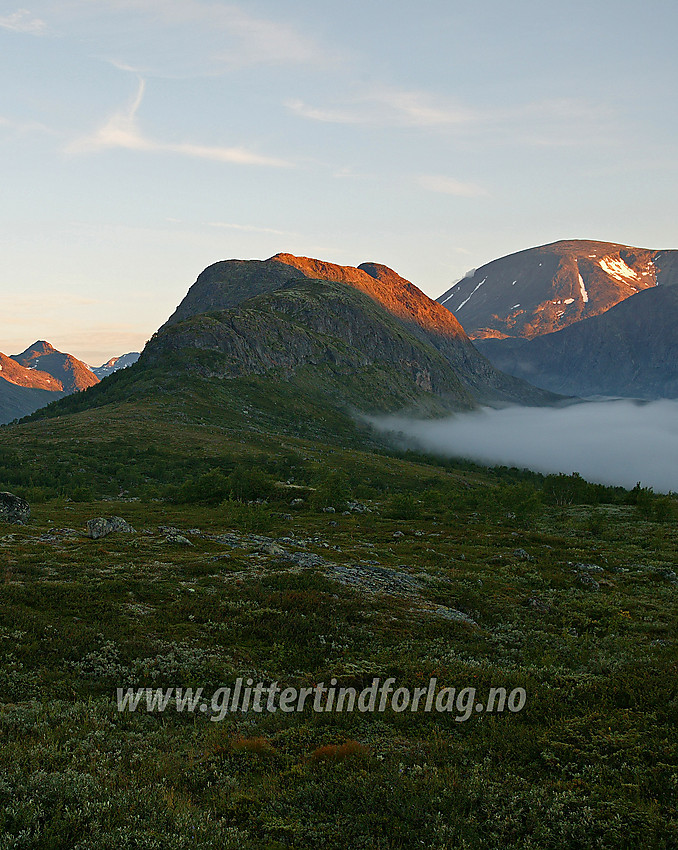 Fra riksvei 51 litt nedenfor Vargebakkan mot Knutshøe (1517 moh.) med den første morgensola på toppen. Morgentåka ligger fortsatt tett over Nedre Leirungen. Besshøe (2258 moh.) ruver bak til høyre.