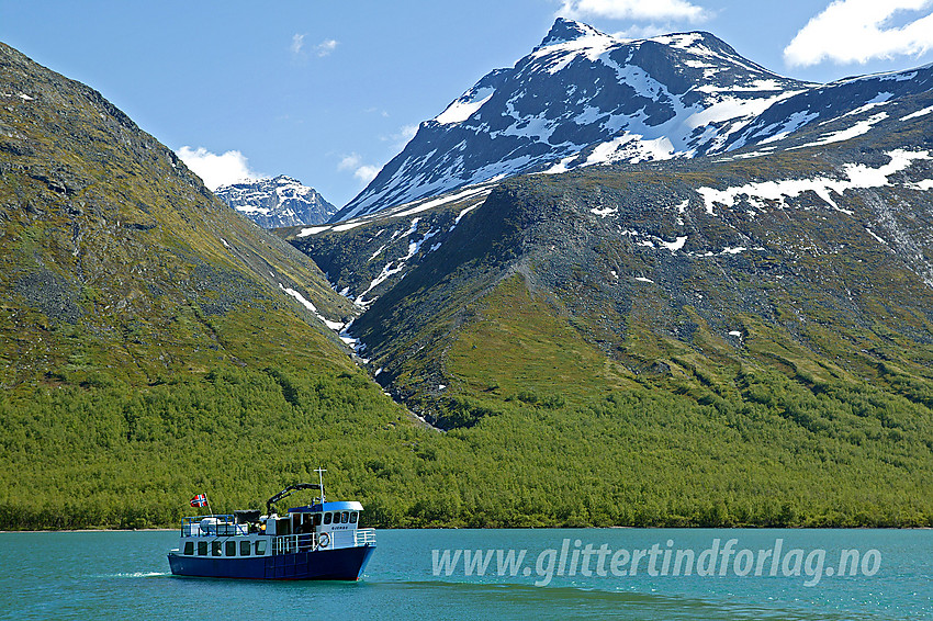 Gjende III trafikkerer Gjende i sommersesongen. Her er båten i ferd med å legge fra brygge ved Gjendebu. I bakgrunnen Nørdre Svartdalspiggen (2137 moh) og munningen på Svartdalen. Stien fra Gjendebu mot Torfinnsbu drar seg bratt opp mot Svartdalen til høyre for elvegjelet.