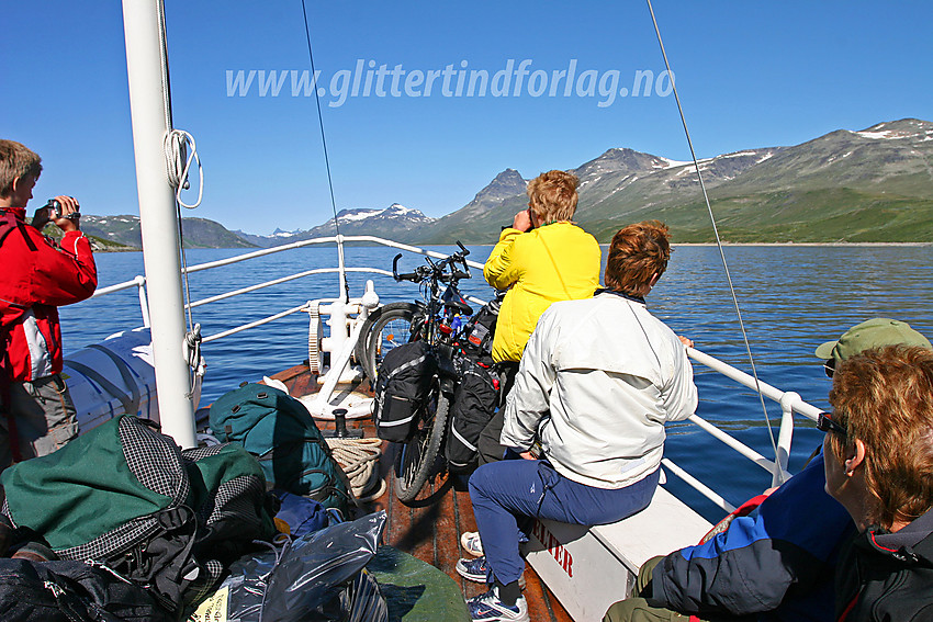 Forventningsfulle fjellturister på m/b Bitihorn, som er på vei fra Bygdin til Torfinnsbu. Panoramaet vestover med Nørdre Kalvehølotinden (2019 moh.), Torfinnstindane (2119 moh.) og Galdebergtinden (2075 moh.) langs Bygdins nordbredd er storartet.