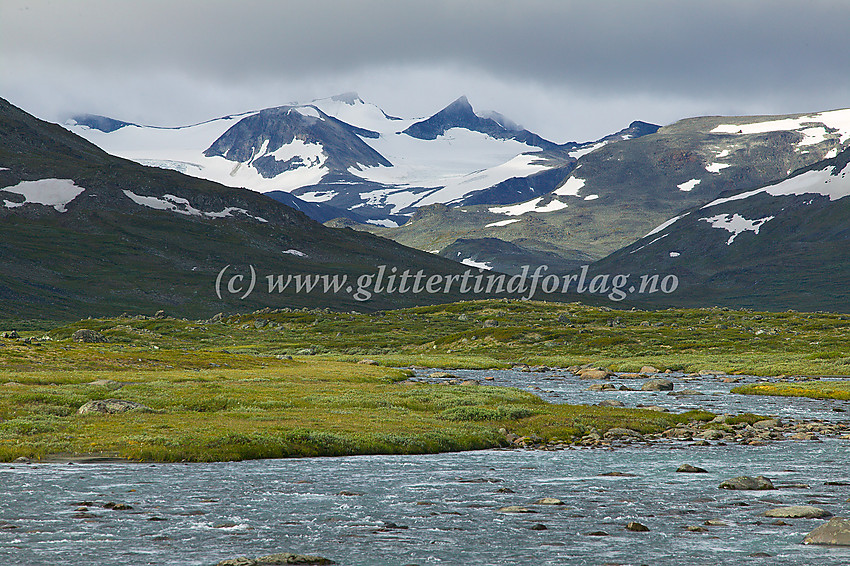 Det kjente Veodalen-panoramaet en gråværsdag. Det er så vidt at Veoitindane stikker toppene sine fram gjennom skyene. den spisse, svarte taggen er Store Veotinden, med Søre Veotinden bak til venstre for denne. Fremst ligger Nørdre Styggehøbreatinden.