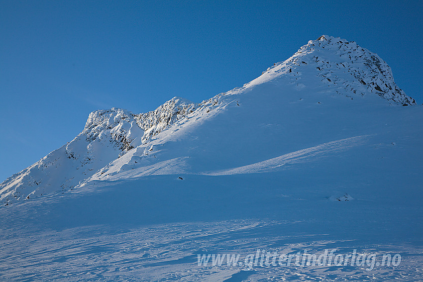 Mjølkedalstinden (2137 moh) sett fra nordvest. Jeg gikk litt ut til venstre og så opp sideryggen delvis i sola opp til toppryggen. En forholdsvis bratt snøbakke.