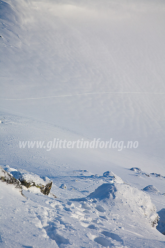 Bratt snøbakke opp til nordvestryggen på Mjølkedalstinden. I bakgrunnen ses skisporene mine nede i bassenget nord for toppen.